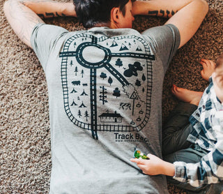Father wearing matching dad and son outfit while playing with toddler boy on carpet for Father’s Day family bonding moment